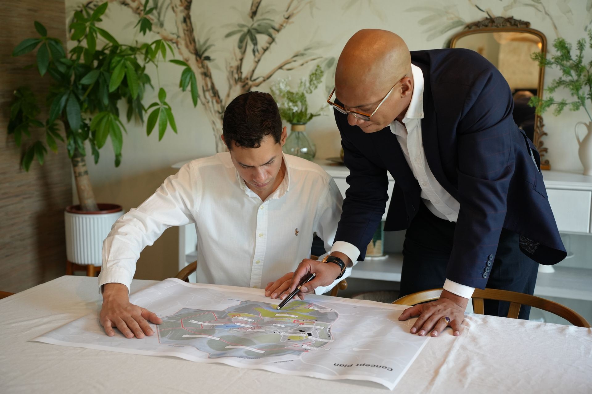 Two individuals discussing a site map on a table in a room with plants and decorative items.