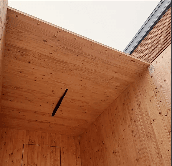 Interior view of a wooden structure with natural wood grain and a narrow vertical slit in the ceiling.