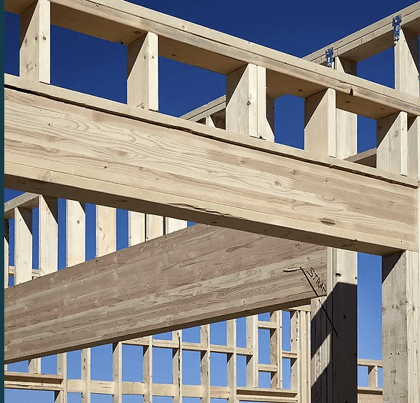 Close-up view of a wooden frame construction with beams and supports, under a clear blue sky.