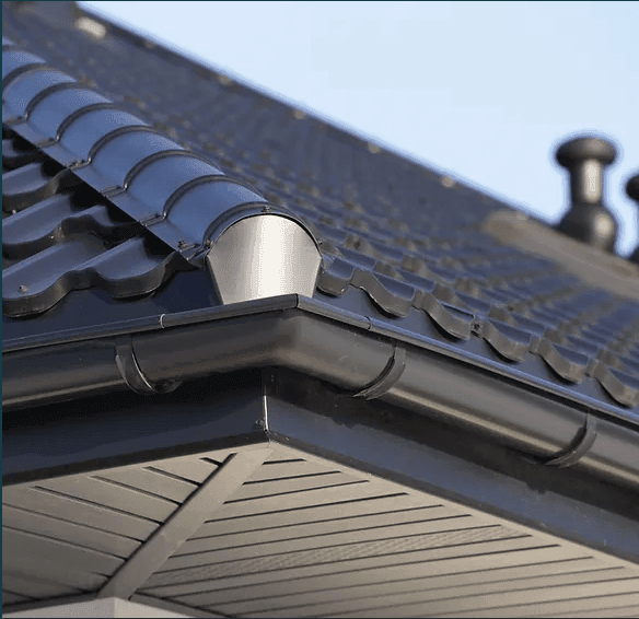 Close-up of a house roof with black metal tiles and rain gutter.